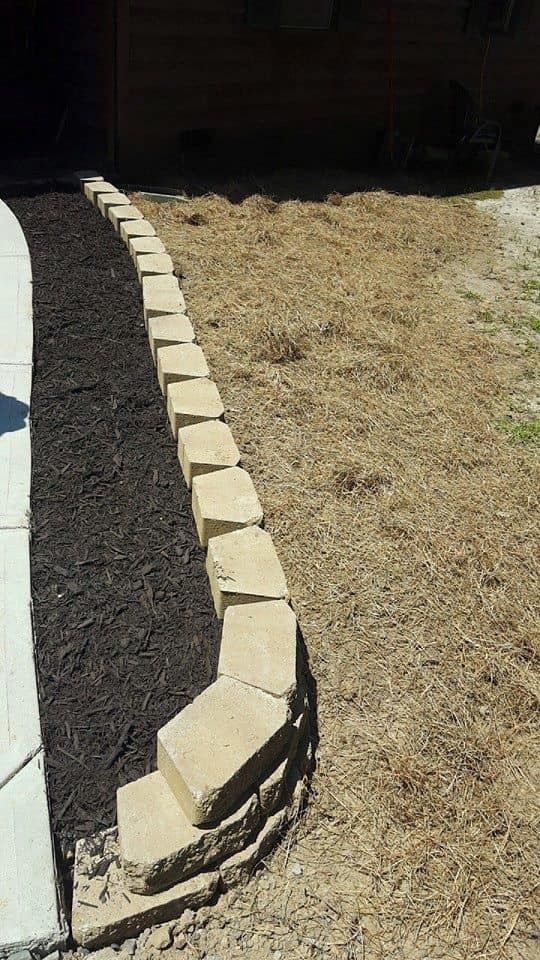 A row of bricks sitting on top of a dirt field next to a sidewalk.