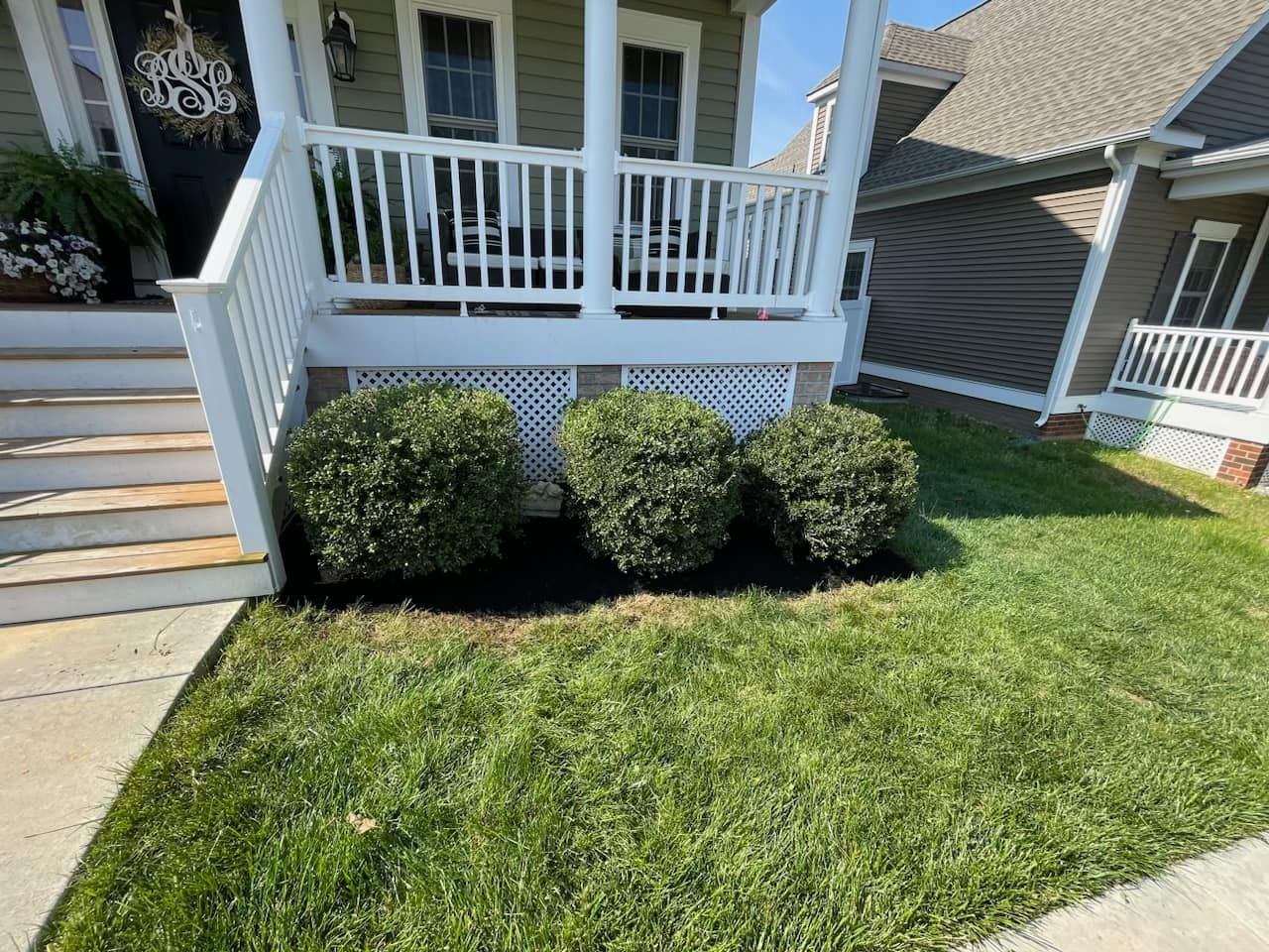 A house with a porch and bushes in front of it.