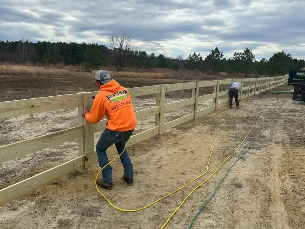 A man in an orange hoodie is working on a wooden fence.