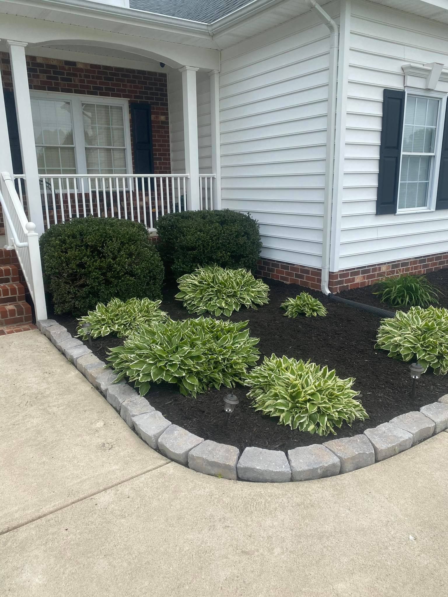 A white house with a brick porch and a garden in front of it.