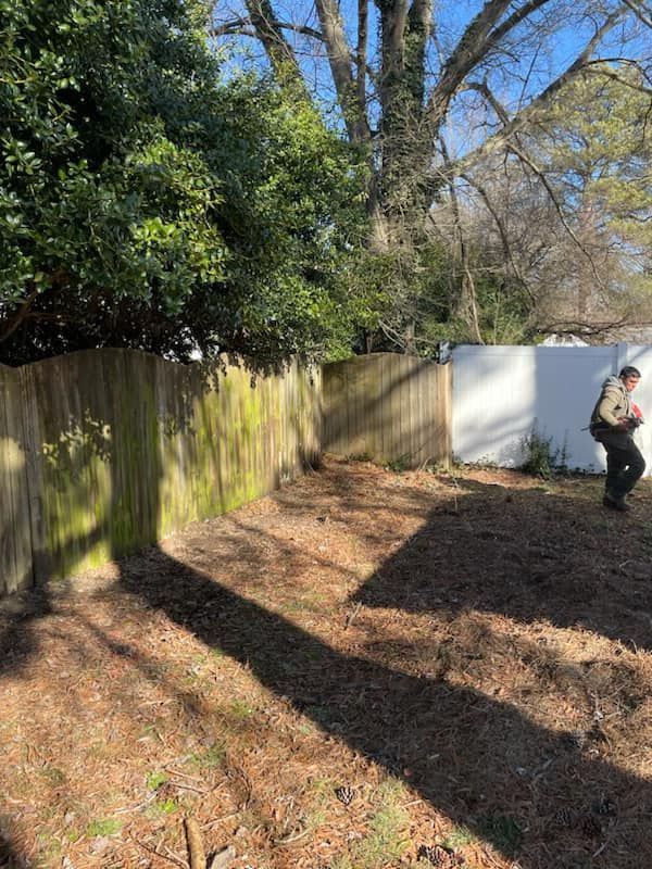 A man is standing in a backyard next to a wooden fence.