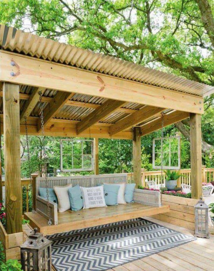 A wooden porch swing with a rug underneath it.