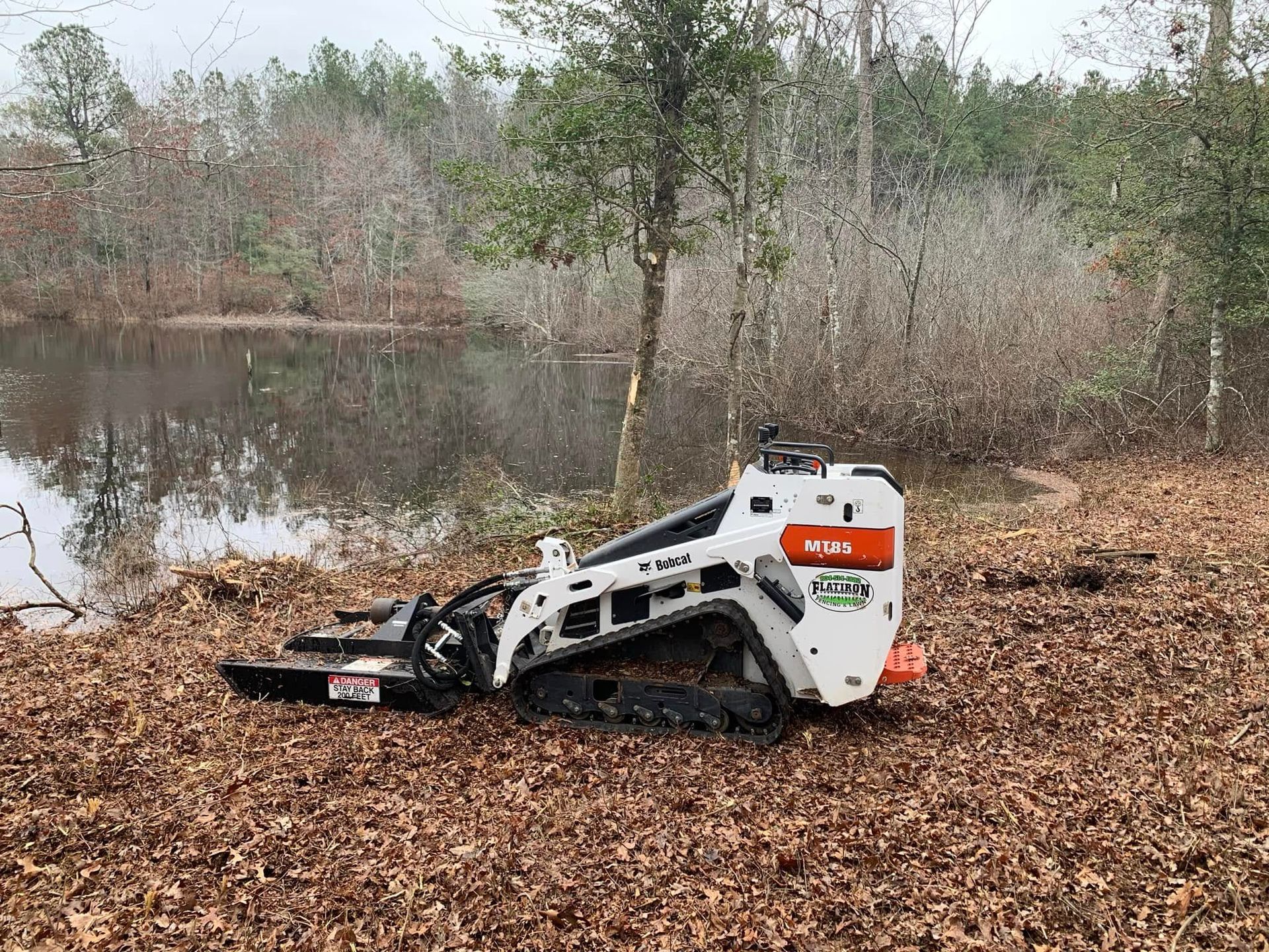 A bulldozer is sitting on top of a pile of leaves next to a body of water.