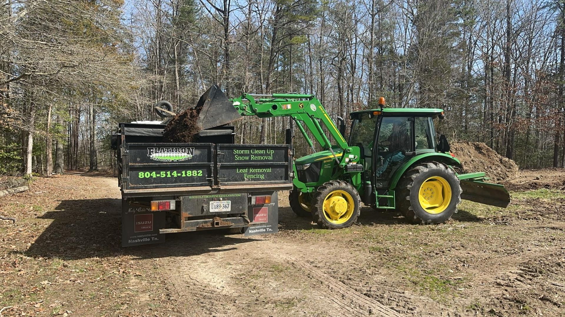 A green tractor is pulling a dumpster on a dirt road.
