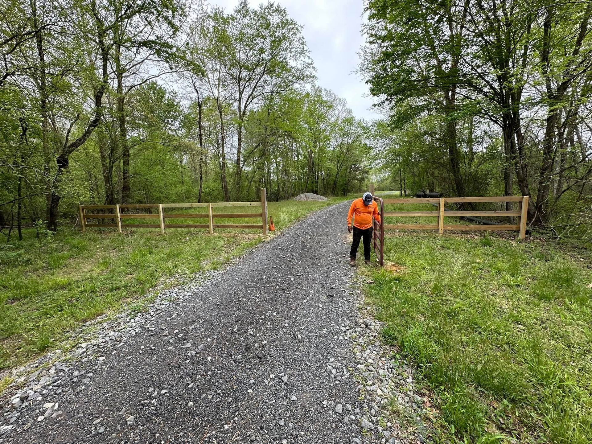 A man is standing on a gravel road next to a wooden fence.