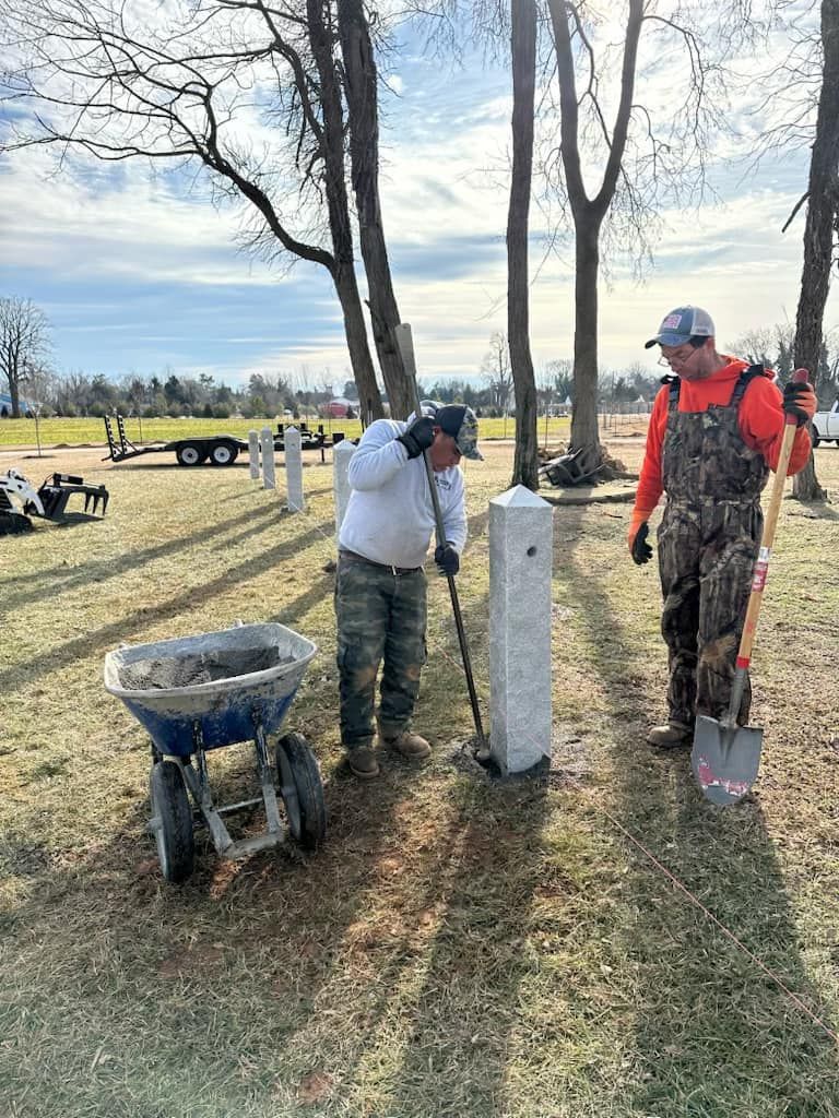 Two men are working in a cemetery with shovels and a wheelbarrow.