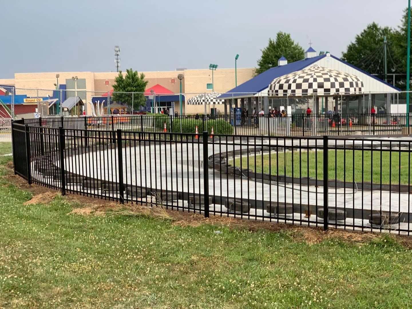 A black fence surrounds a go kart track in a park.