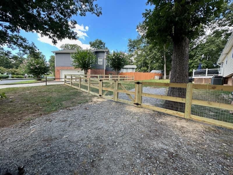 A wooden fence surrounds a gravel driveway in front of a house.