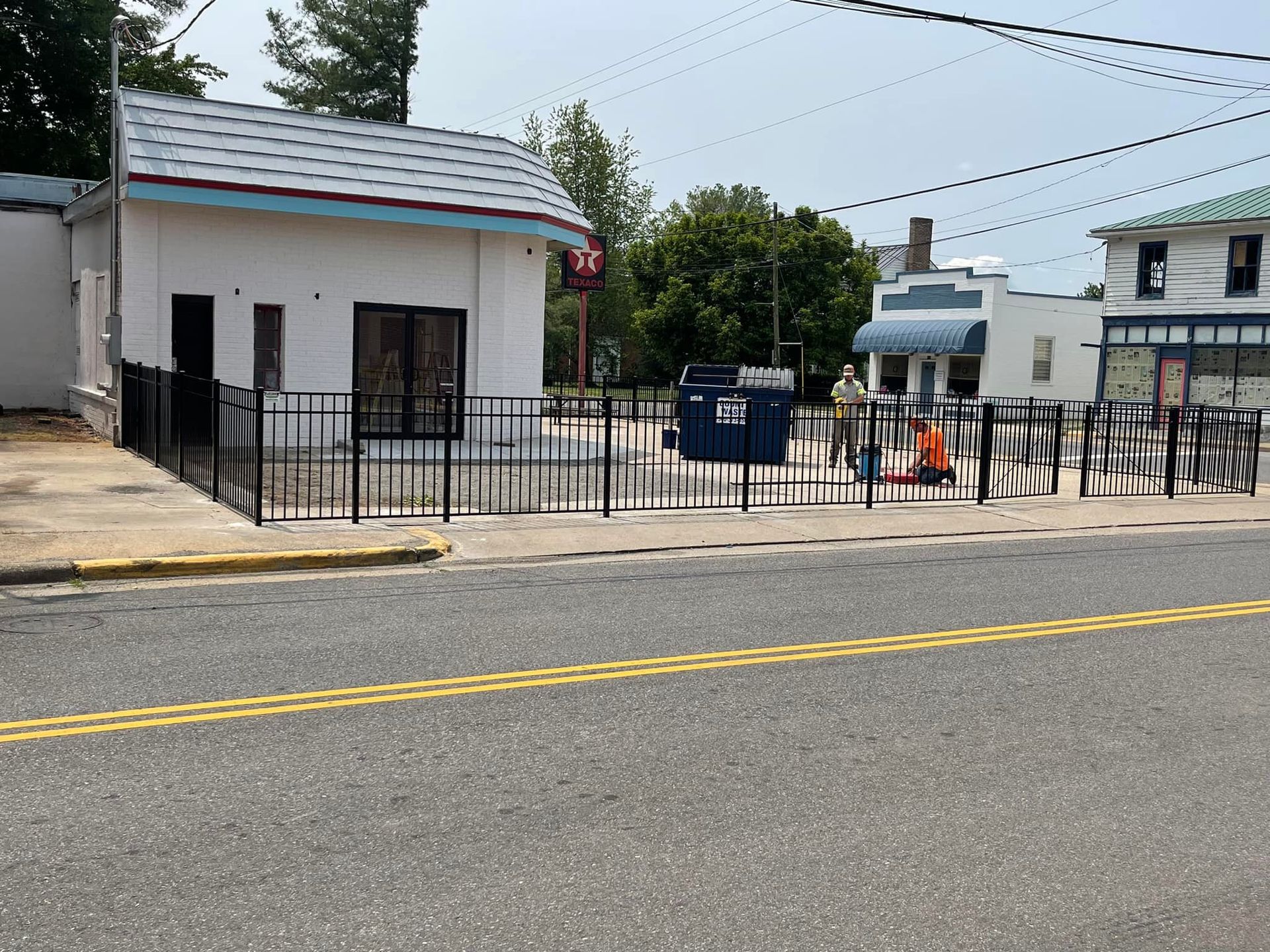 A fence surrounds a small white building on the side of the road