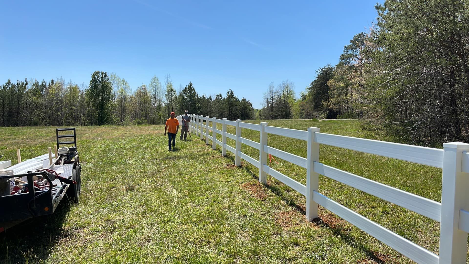 A man is standing in a field next to a white fence.