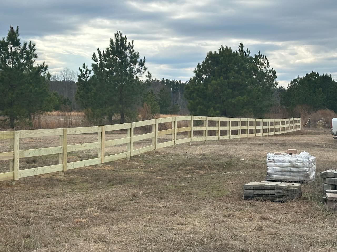 A wooden fence in a field with trees in the background
