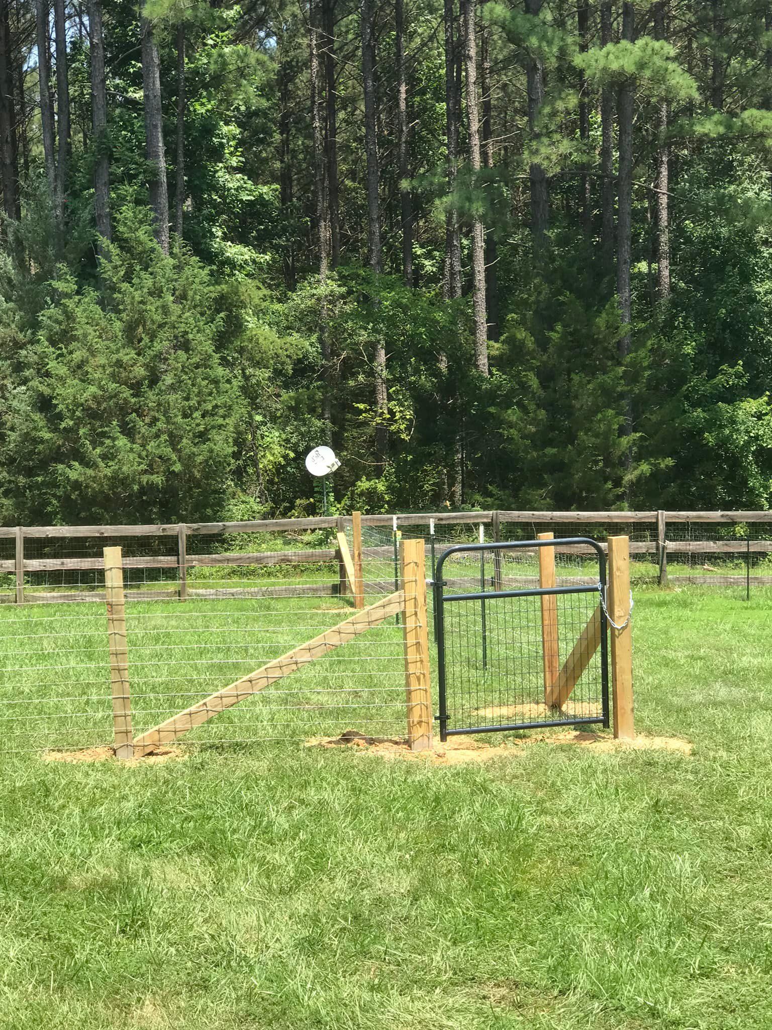 A wooden fence with a gate in the middle of a grassy field.