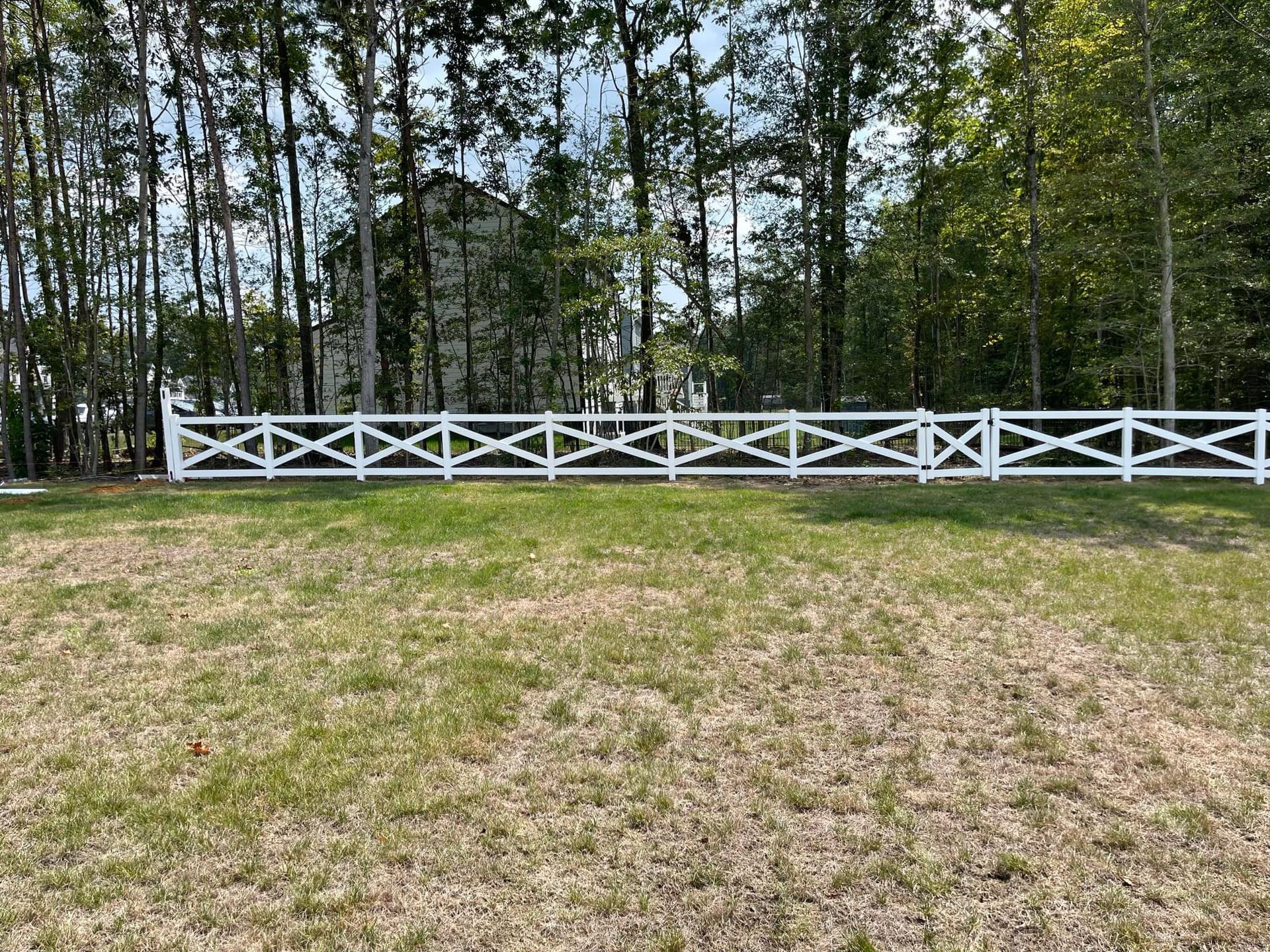 A white fence surrounds a grassy field with trees in the background.