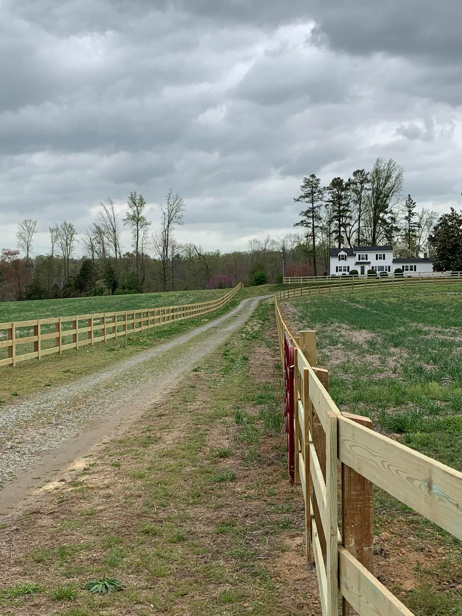 A wooden fence along a dirt road with a house in the background.