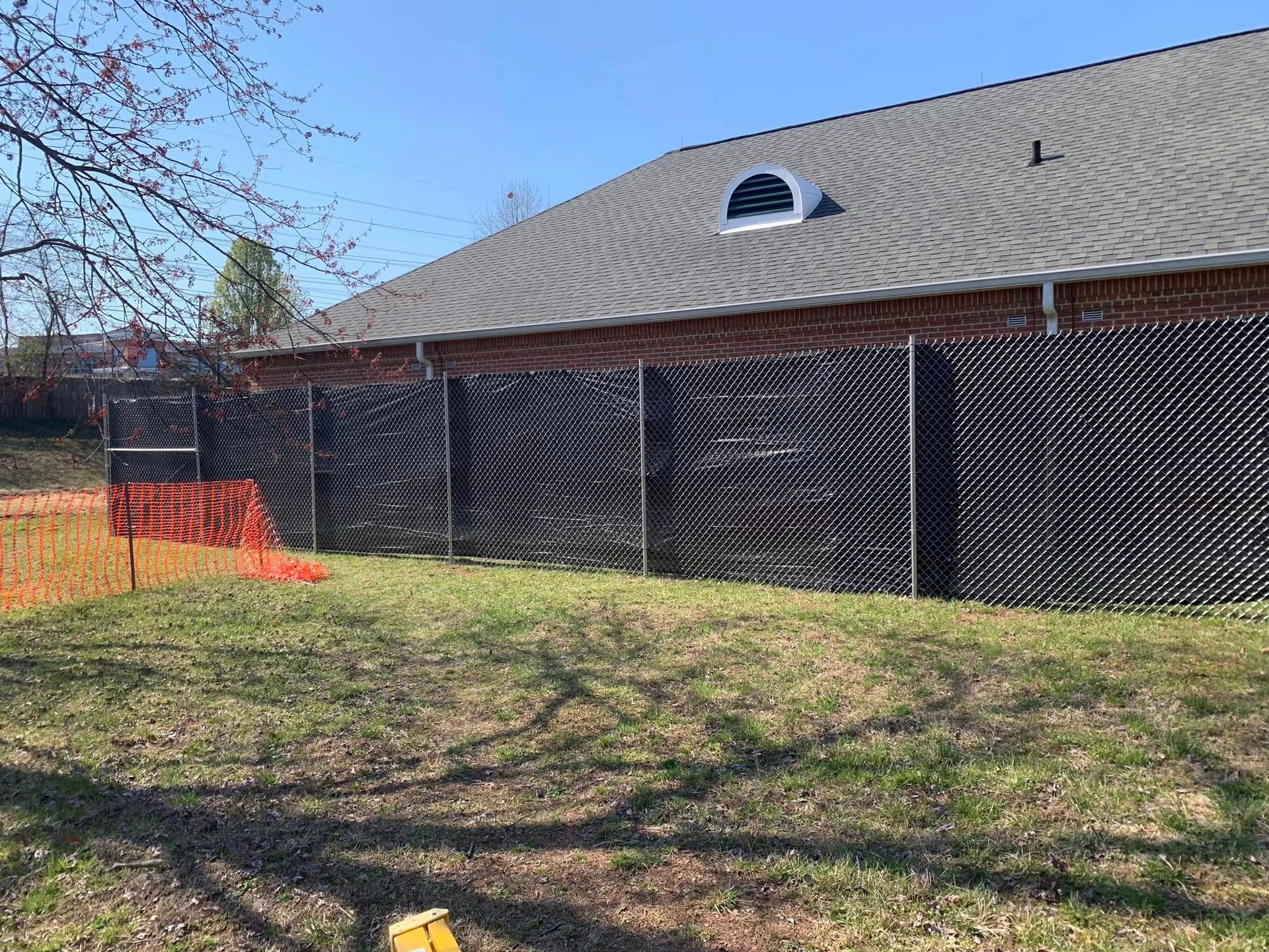 A fence is surrounding a grassy field in front of a brick building.