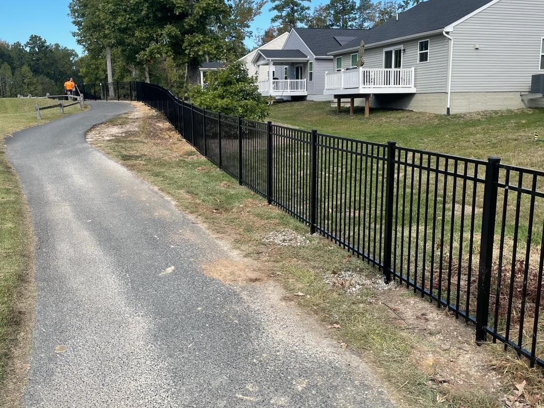 A black wrought iron fence along a gravel road next to a house.