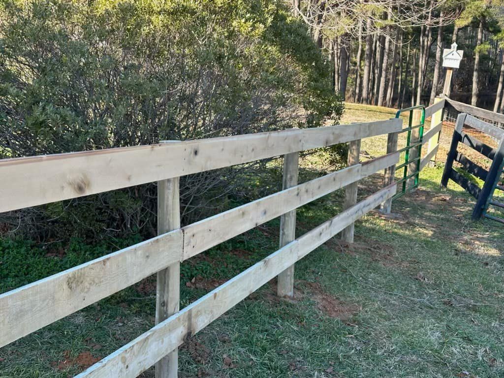 A wooden fence is surrounded by grass and trees in a field.