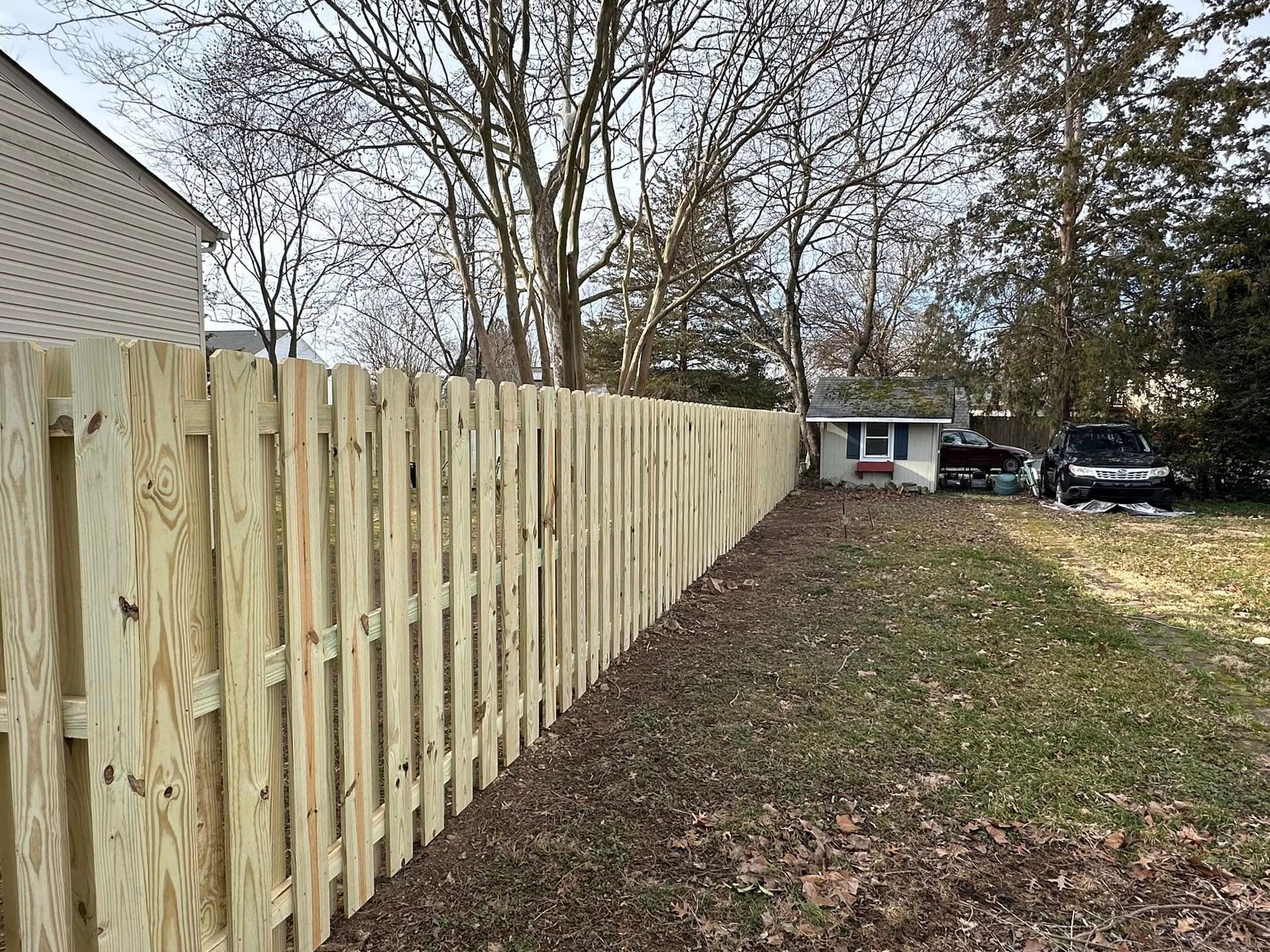 A wooden fence is surrounding a house in a backyard.