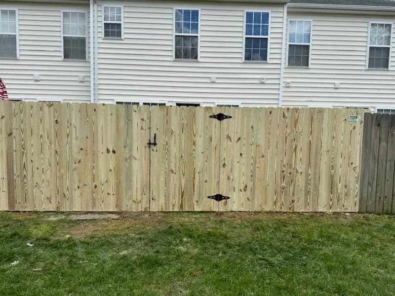 A wooden fence with a gate is in the backyard of a house.