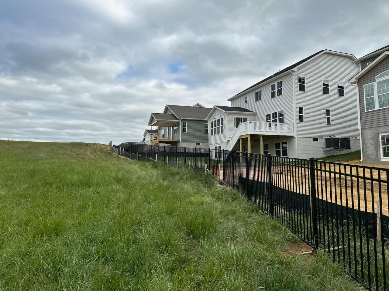 A fence surrounds a grassy field in front of a row of houses.