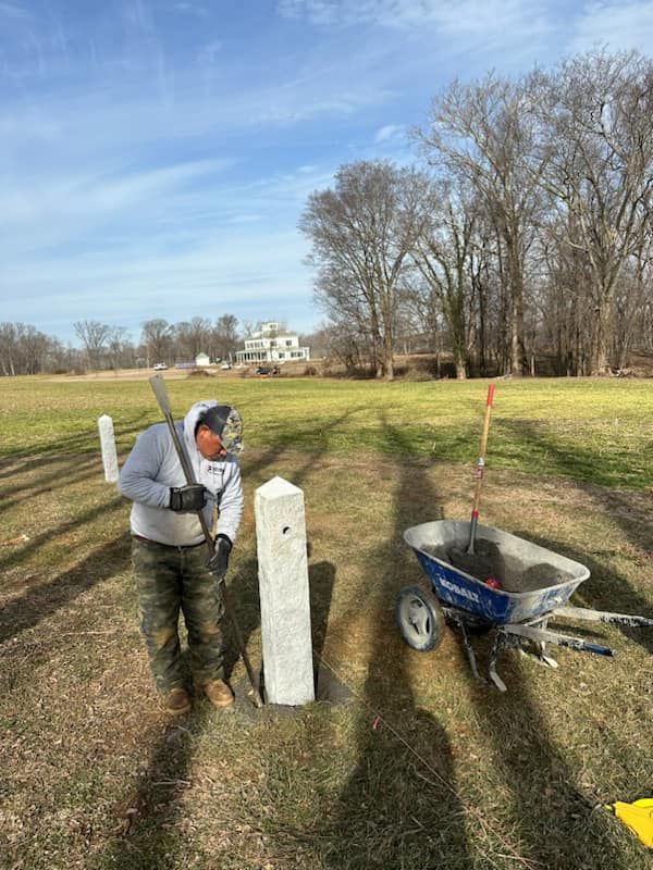 A man is standing next to a wheelbarrow in a field.