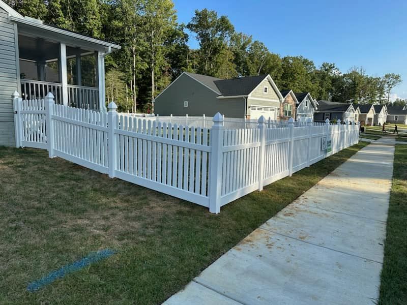A white picket fence surrounds a yard in front of a house.