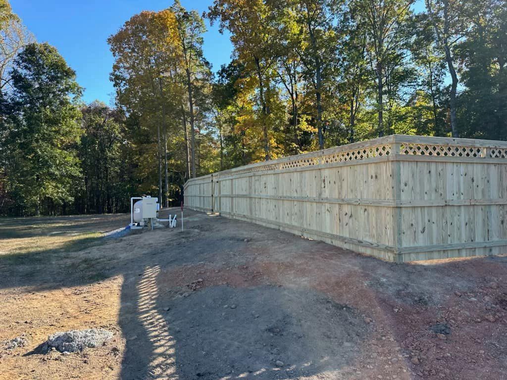 A wooden fence surrounds a dirt road in the middle of a forest.