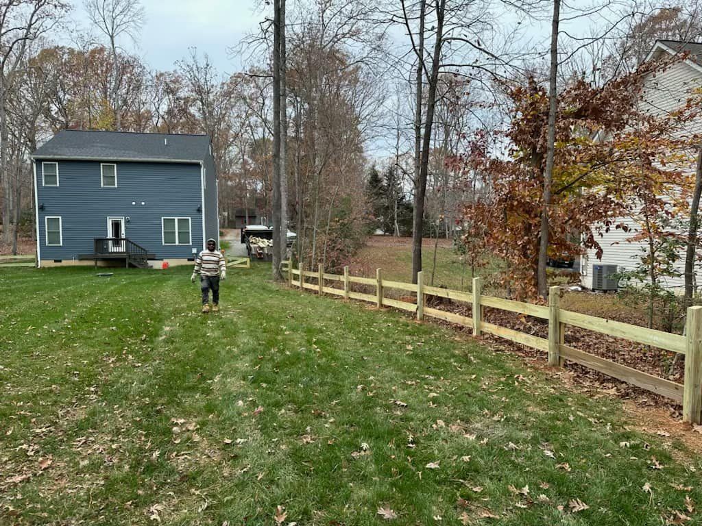 A man is walking along a wooden fence in front of a house.