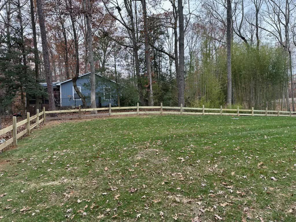 A wooden fence surrounds a lush green field with a blue house in the background.
