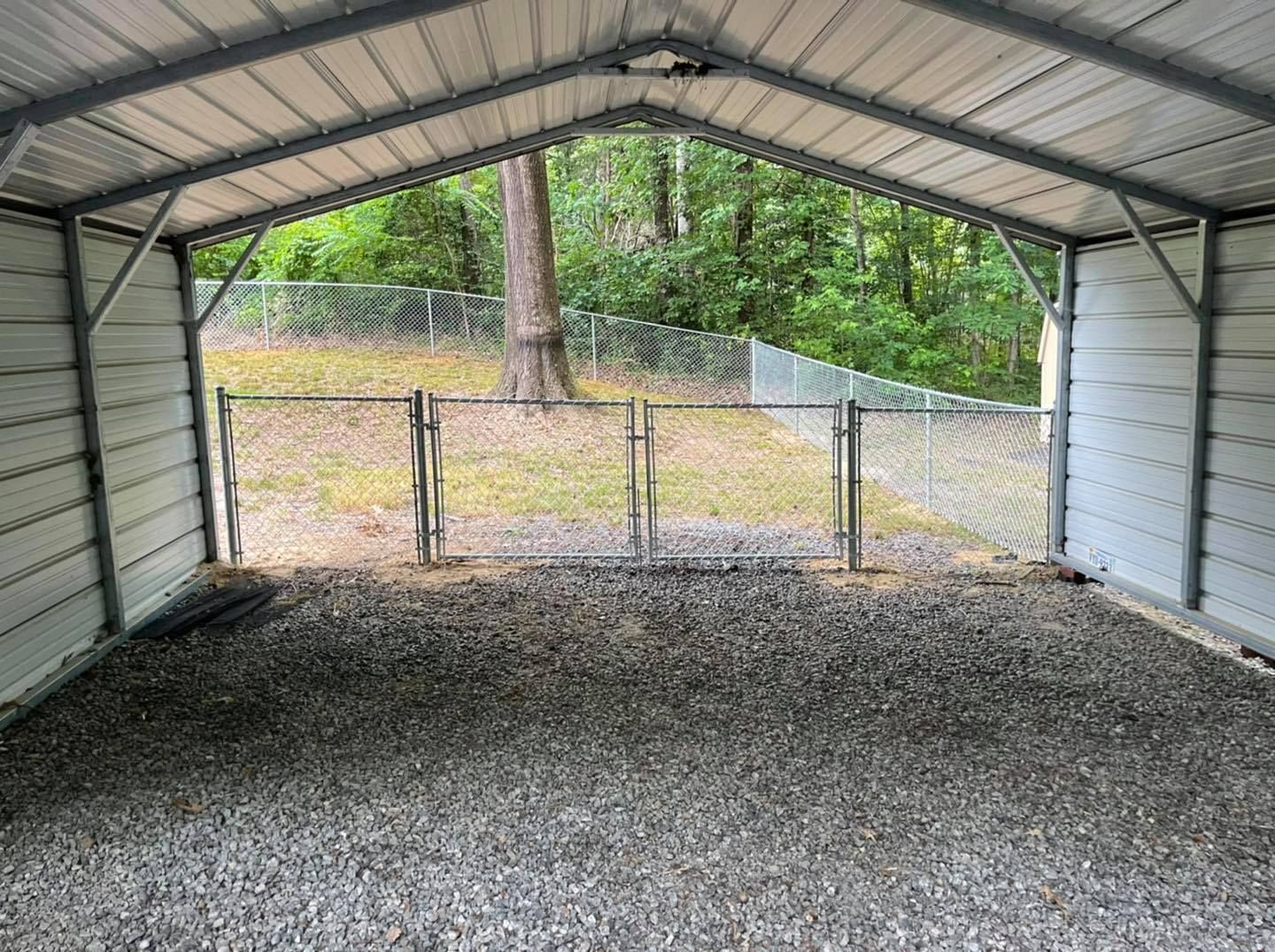 An empty carport with a chain link fence and gravel in front of it.