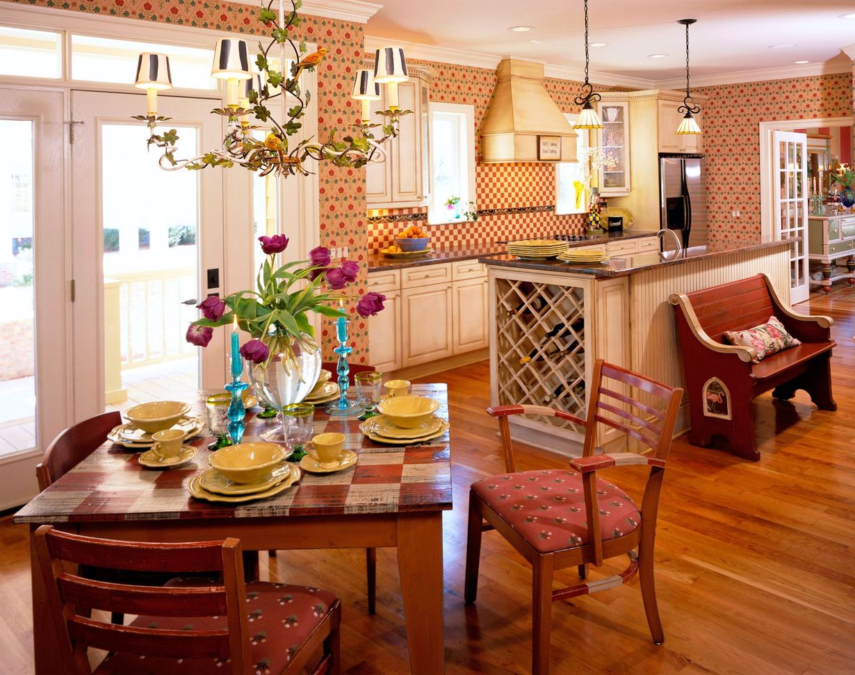 Bright kitchen and dining area with wooden table, flowers, wine rack, and warm orange decor