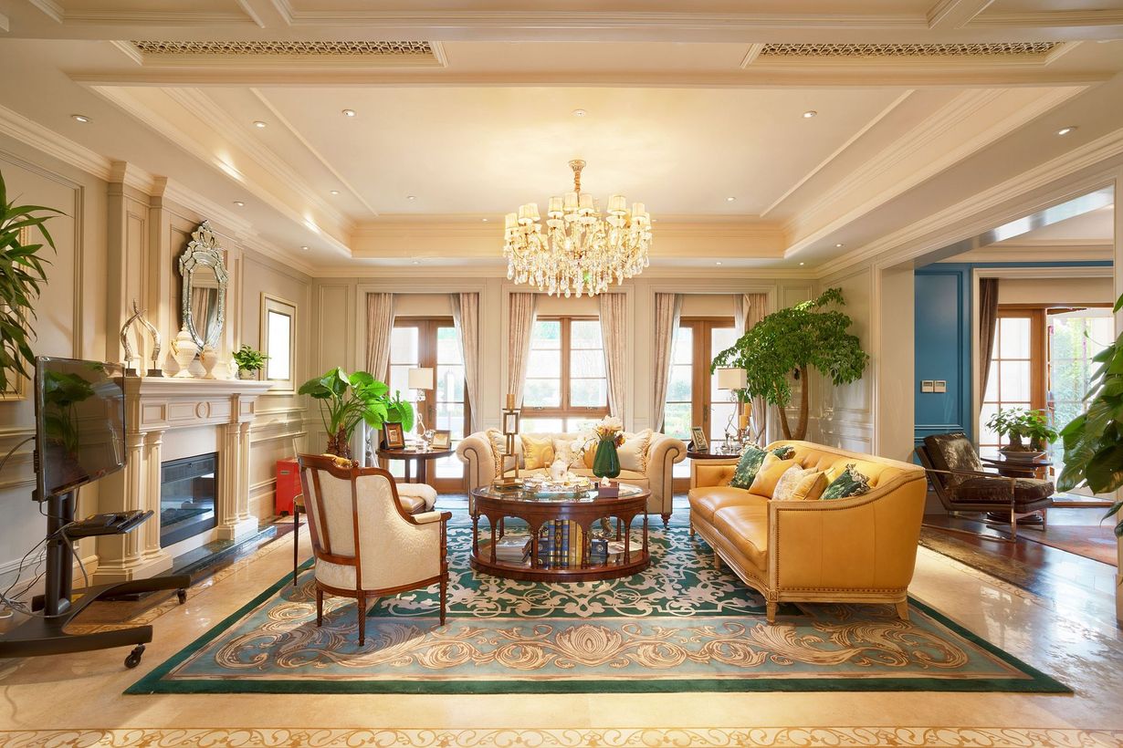 Elegant living room with chandelier, fireplace, gold sofa, and large windows overlooking greenery