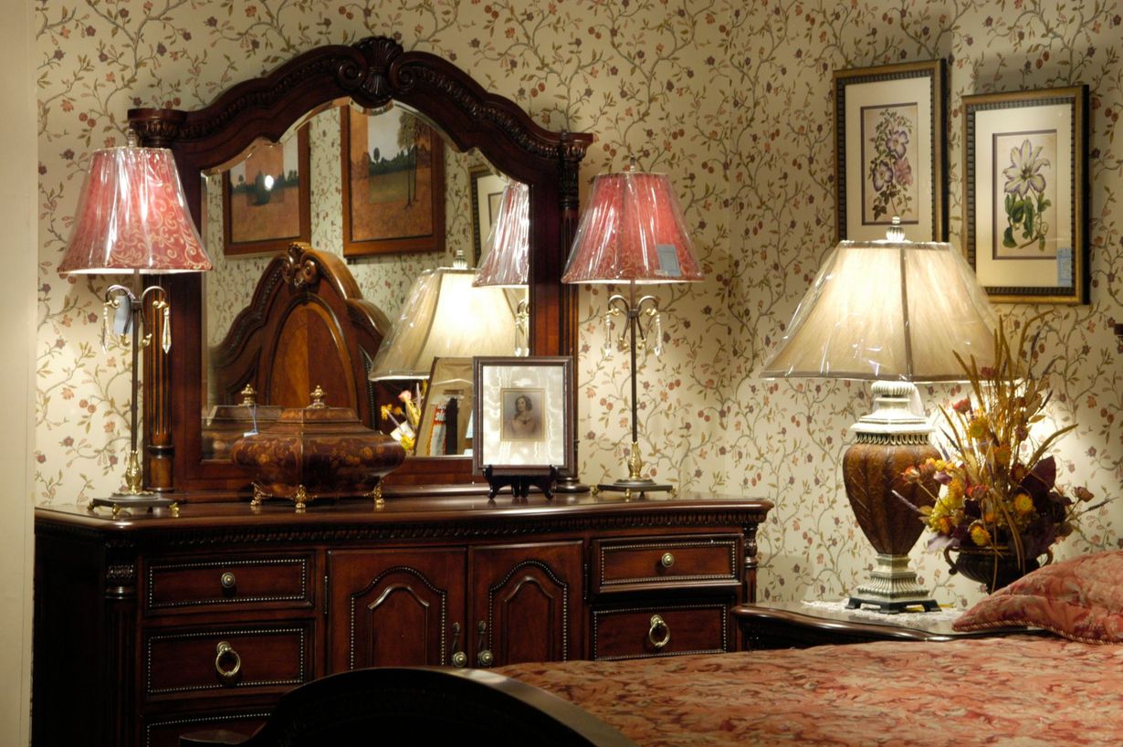 Vintage bedroom with ornate dresser, mirror, table lamps, and a bed with floral bedding
