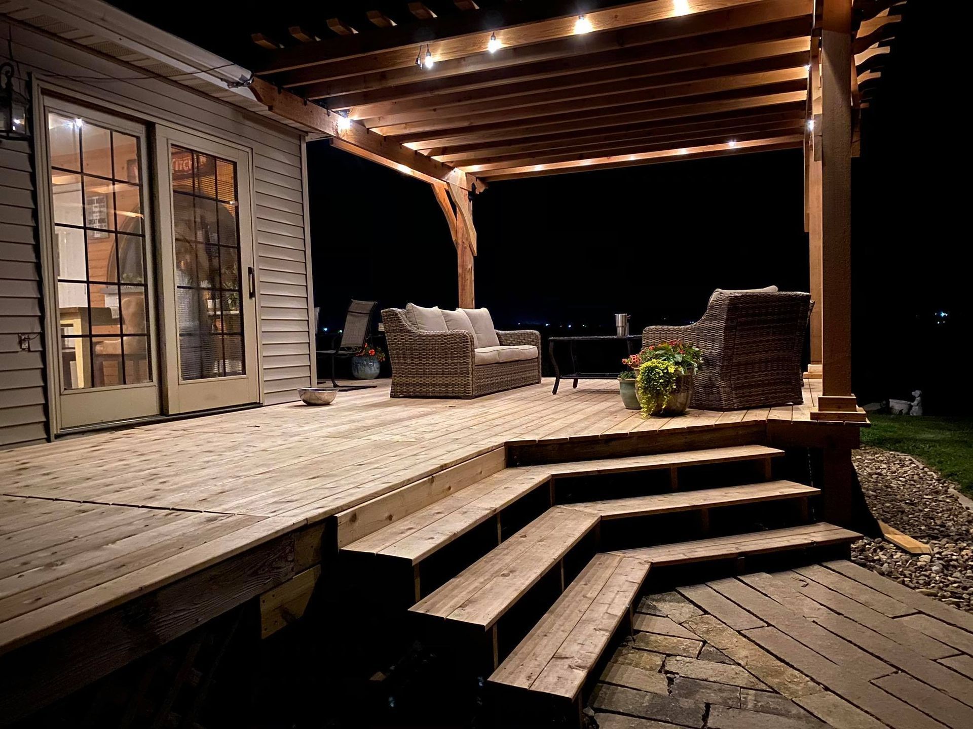 A wooden deck with stairs and a pergola at night.