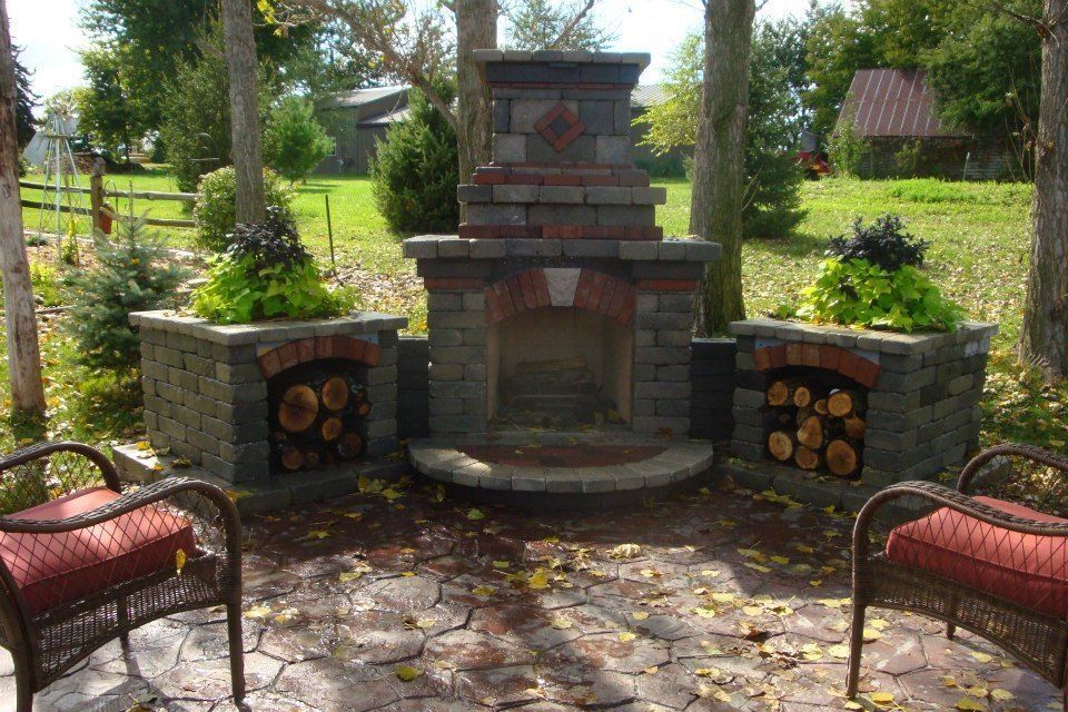 Outdoor fireplace with wood storage and planters, surrounded by trees and seating.