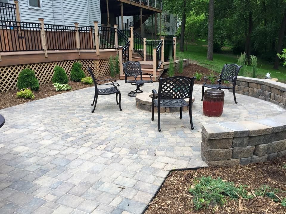 Stone patio with fire pit, seating, and a retaining wall near a wooden deck.