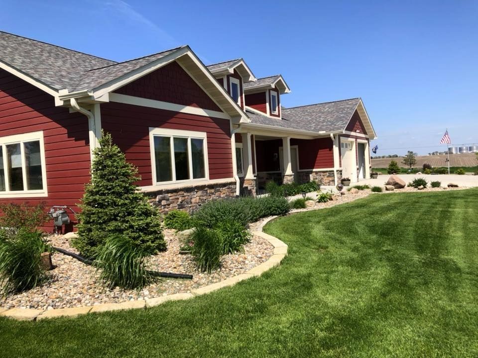 Red house with stone accents, lush green lawn, and landscaping under a blue sky.