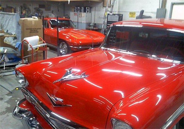 Red classic car in a garage with another red car in the background; shiny paint, chrome details.
