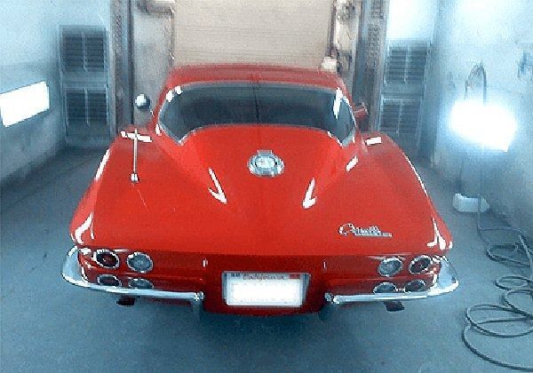 Red classic Corvette rear view in a shop. Chrome bumpers and tail lights.