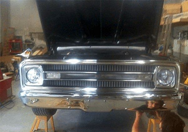 Black classic truck, hood open, chrome grill, mechanic working underneath.