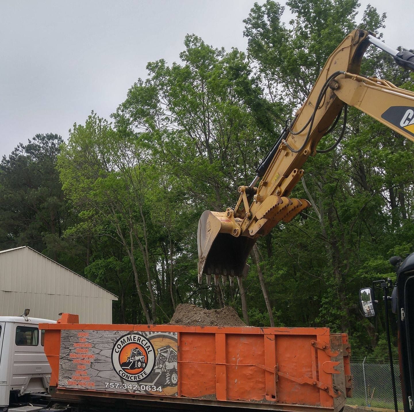 Yellow excavator dumping debris into an orange truck bed. Trees are in the background.