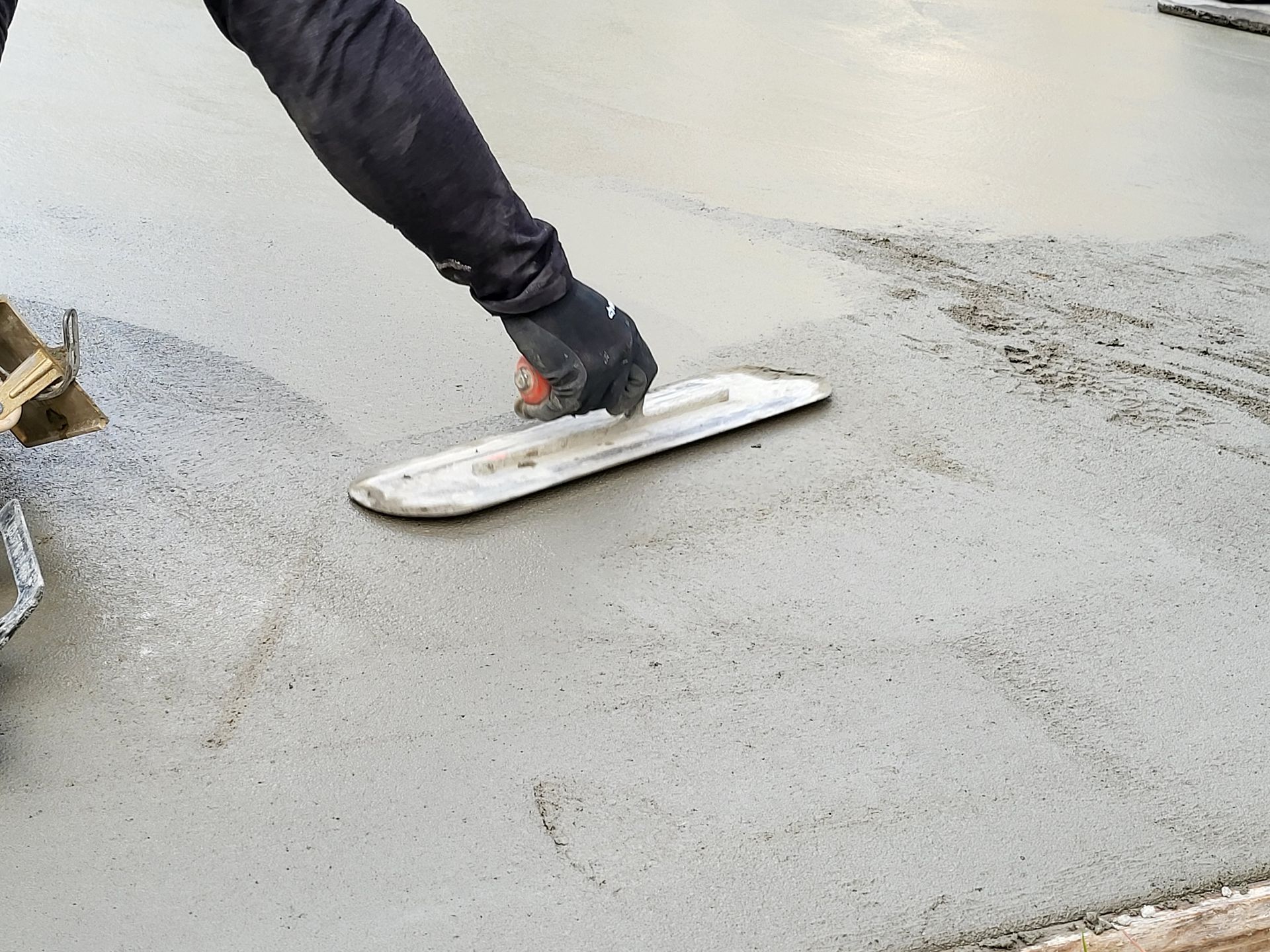 Person smoothing wet concrete with a trowel outdoors.