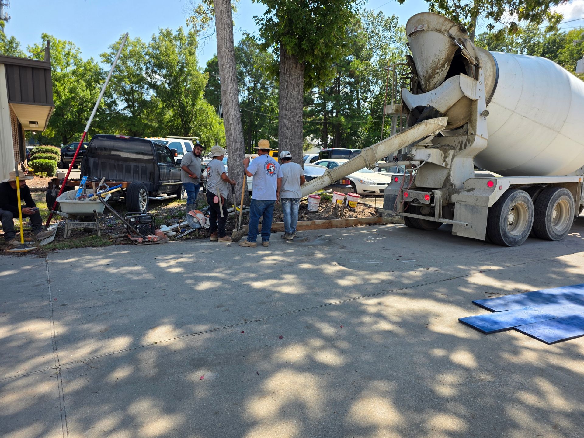 Cement truck pouring concrete near trees, construction workers standing by.