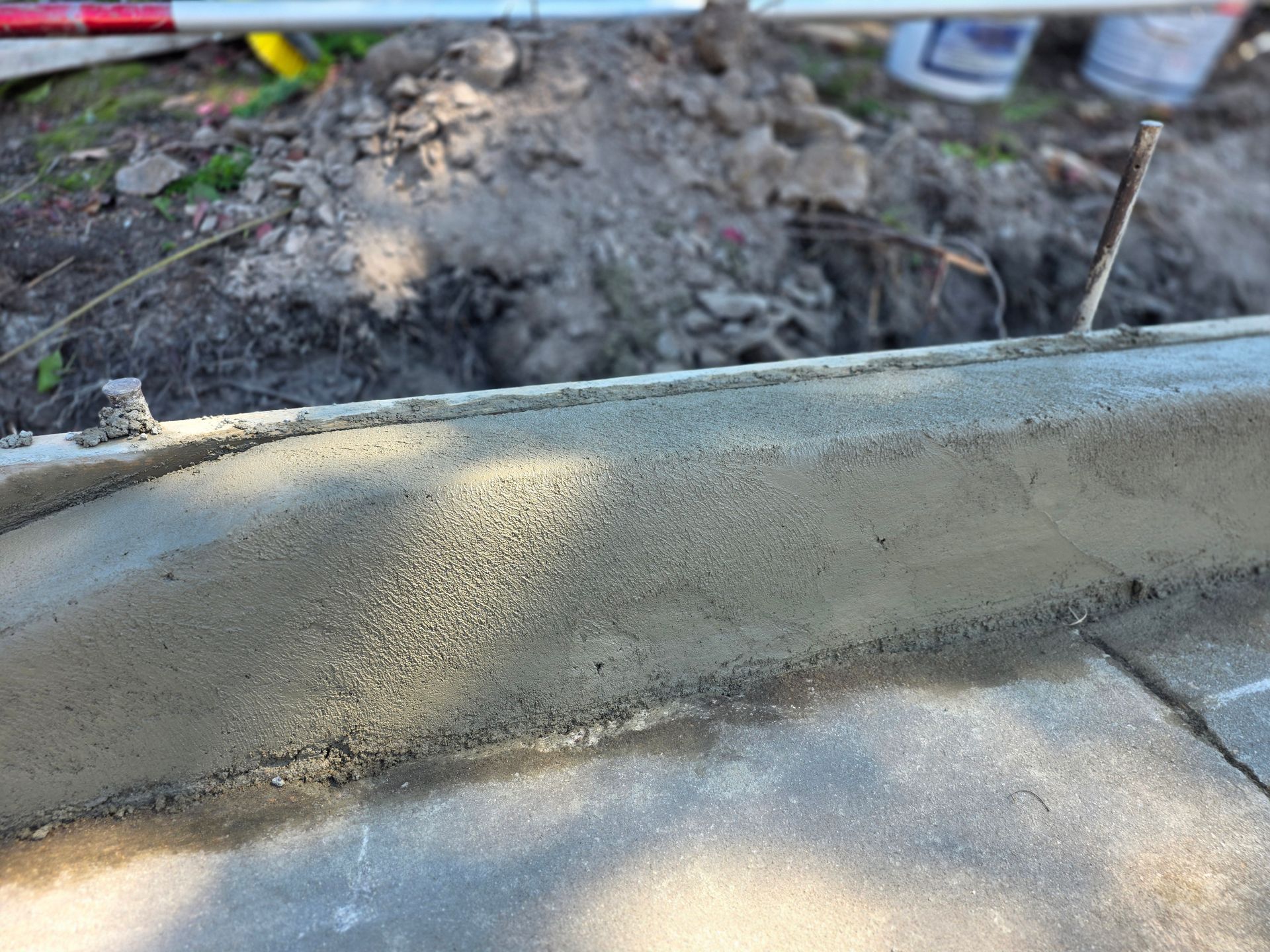 Freshly poured concrete curb next to a sidewalk and dirt.