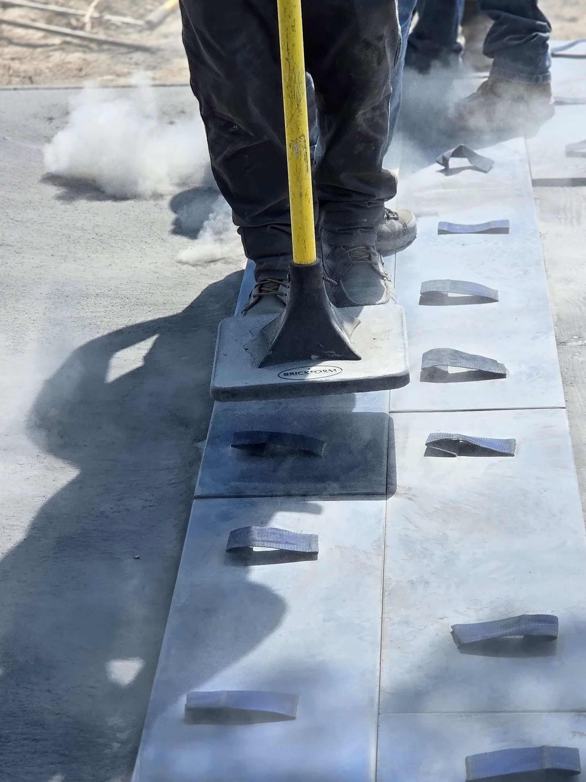 Person using a tool on a line of grey rectangular pavers, producing visible steam.
