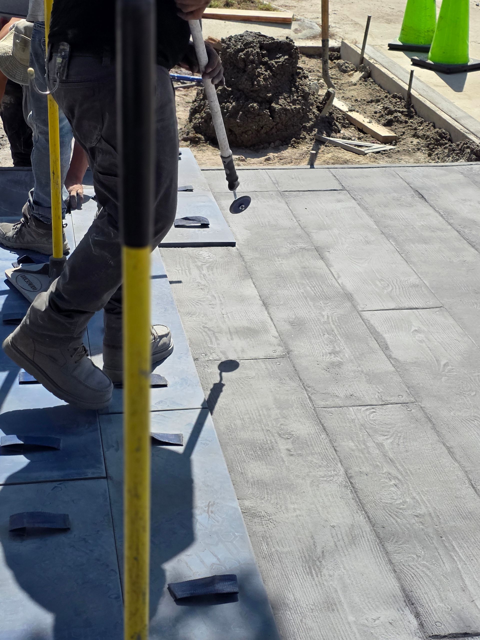 Construction worker installing paving tiles, using a tool to tap them into place. Outdoors, sunny.