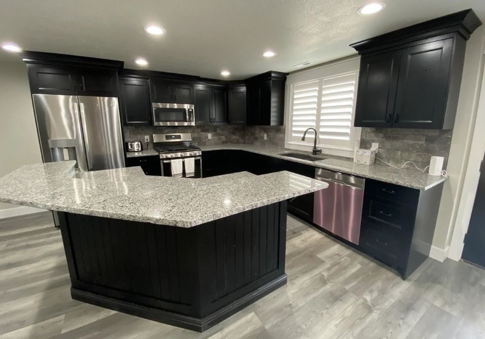 Black kitchen with granite countertops and stainless steel appliances; island with bar seating.