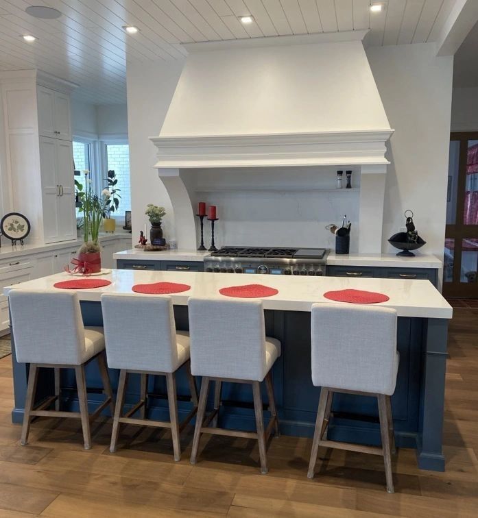 Kitchen with blue island, white countertops, and four bar stools with white seats, wood floors, and a range.