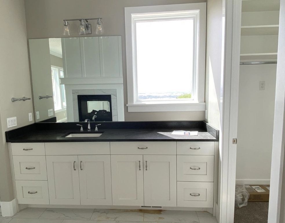 Bathroom with white cabinets, black countertop, large mirror, window, and walk-in closet.