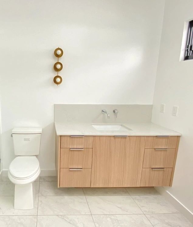 Modern bathroom with light wood floating vanity, white countertop, and toilet. White walls.
